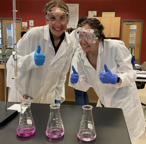 two students in chem lab with thumbs up