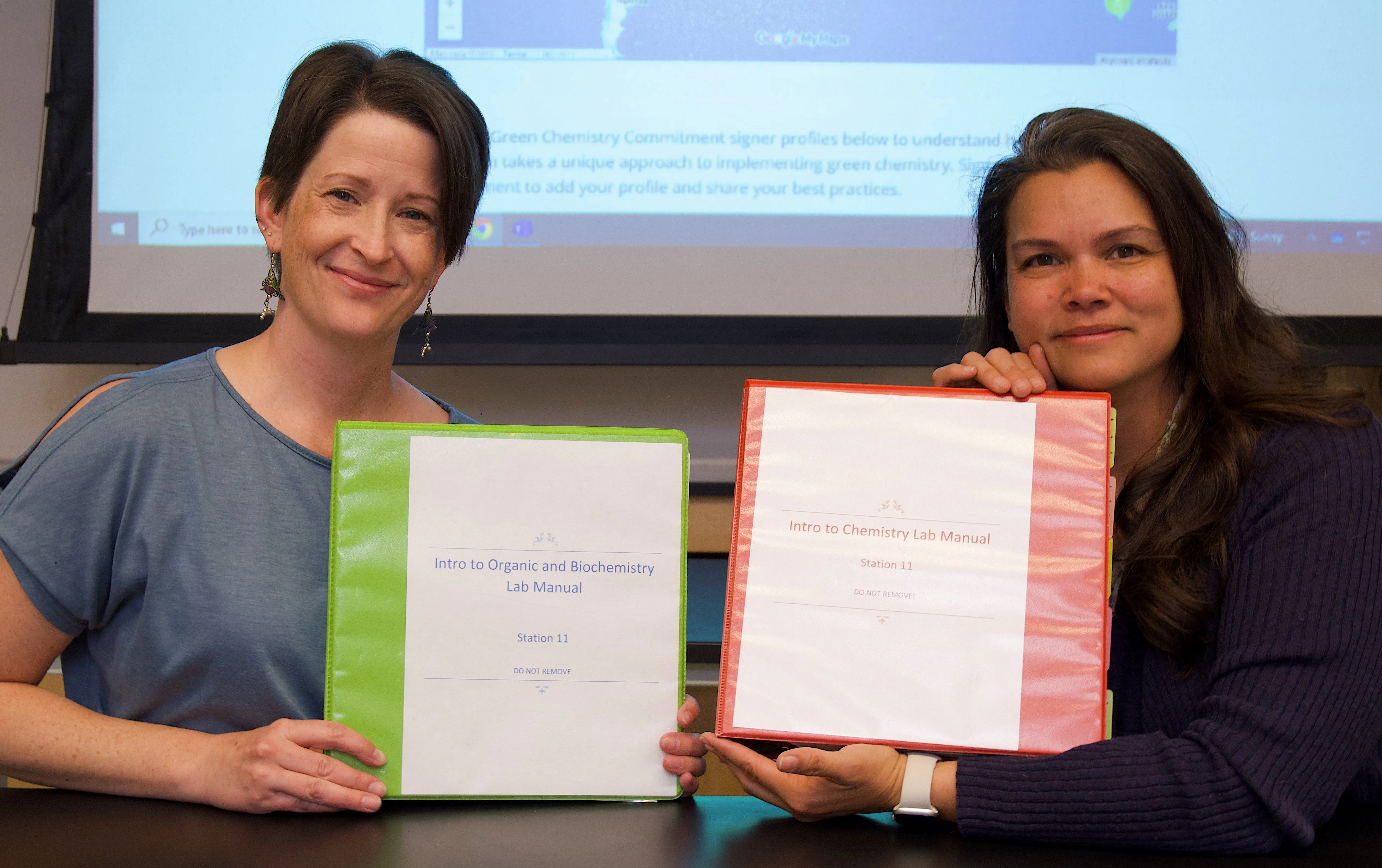 Instructors holding up binders containing lab manuals they created